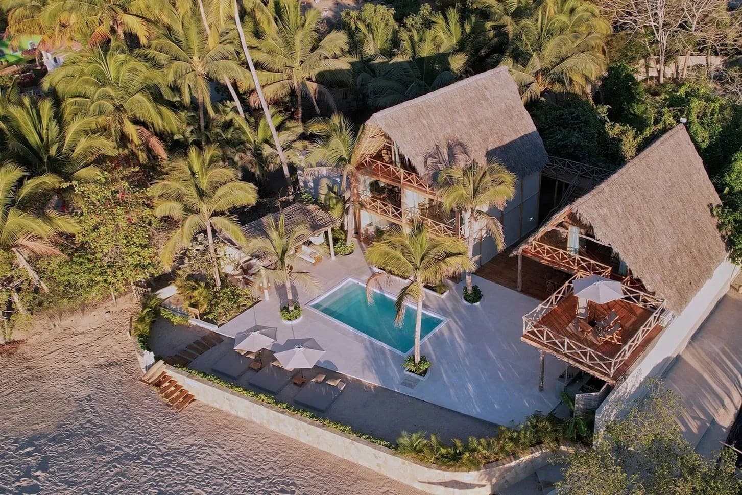 An ocean-front retreat with thatched-roof palapas, a pool, and palms, reached by boat